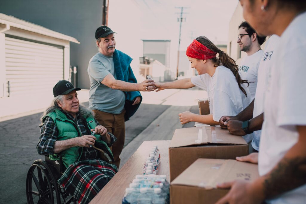 Volunteers distribute water and supplies to people outdoors, promoting community support and kindness.
